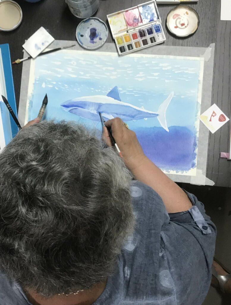 une femme peint à l'aquarelle un requin sous l'eau pendant un atelier d'aquarelle de Phil de Lov
